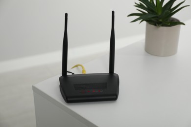 Photo of Modern Wi-Fi router on white table in room. Space for text