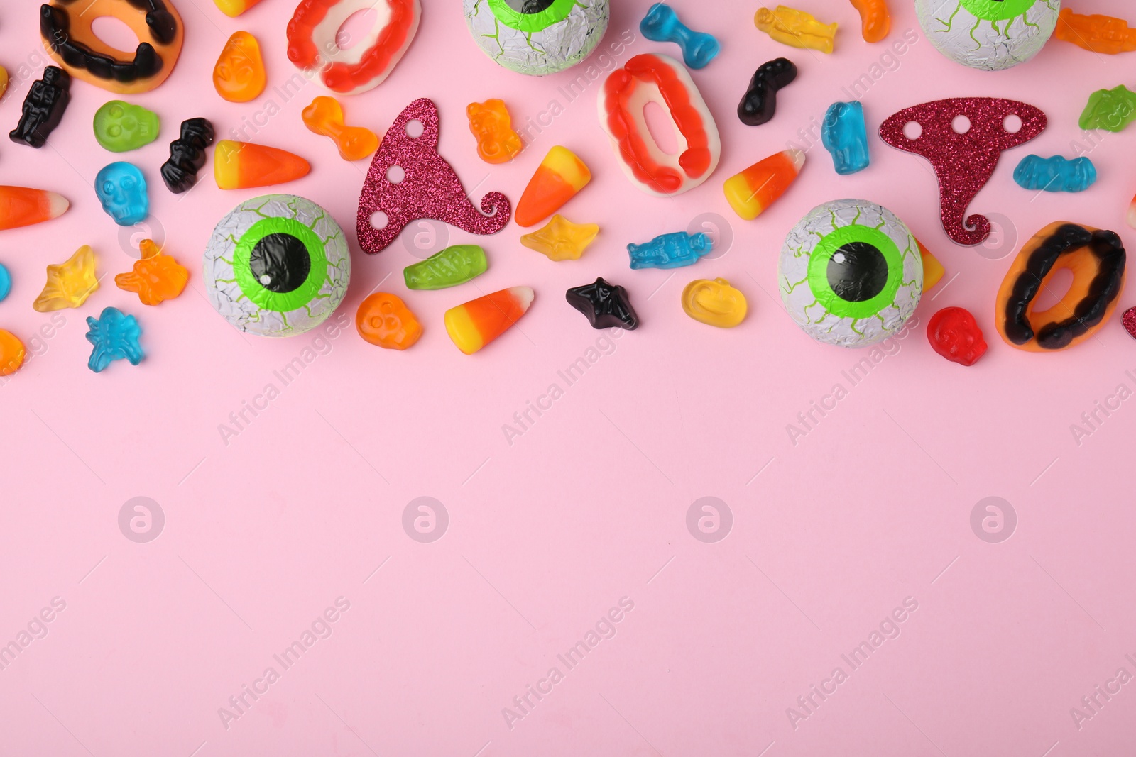 Photo of Tasty colorful jelly candies and Halloween decorations on pink background, flat lay. Space for text