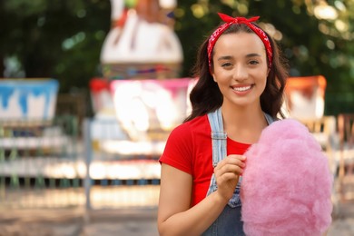 Photo of Stylish young woman with cotton candy at funfair, space for text