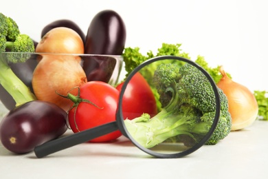Photo of Different fresh vegetables and magnifying glass on table, closeup. Poison detection