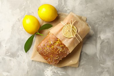 Photo of Wrapped tasty lemon cake with glaze and citrus fruits on light grey textured table, top view