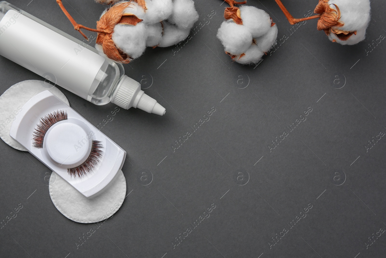 Photo of Bottle of makeup remover, cotton flowers, pads and false eyelashes on grey background, flat lay. Space for text