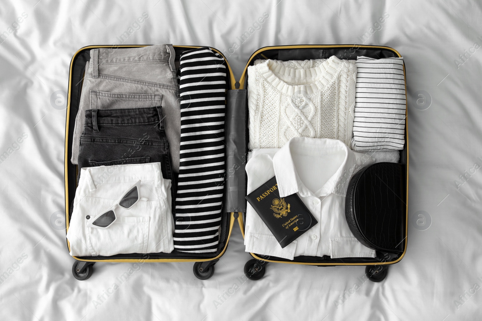 Photo of Open suitcase with clothes, passport and accessories on bed, top view