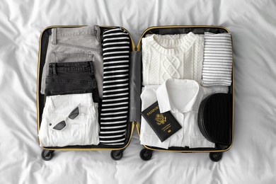 Photo of Open suitcase with clothes, passport and accessories on bed, top view