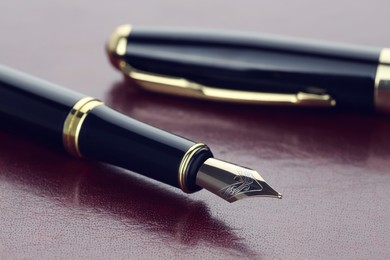 Stylish fountain pen and cap on leather surface, closeup