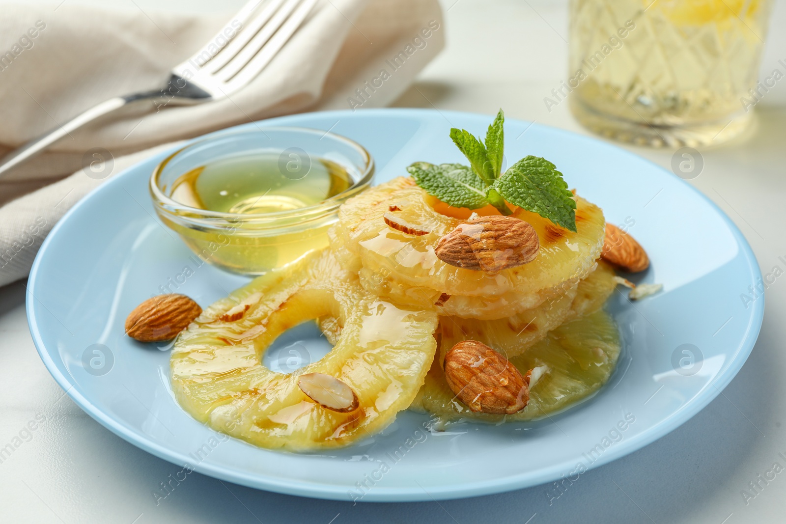 Photo of Tasty grilled pineapple slices served with mint and almonds on white table, closeup