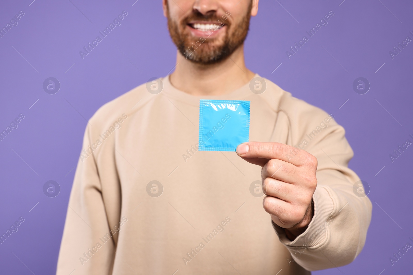 Photo of Man holding condom on purple background, closeup. Safe sex