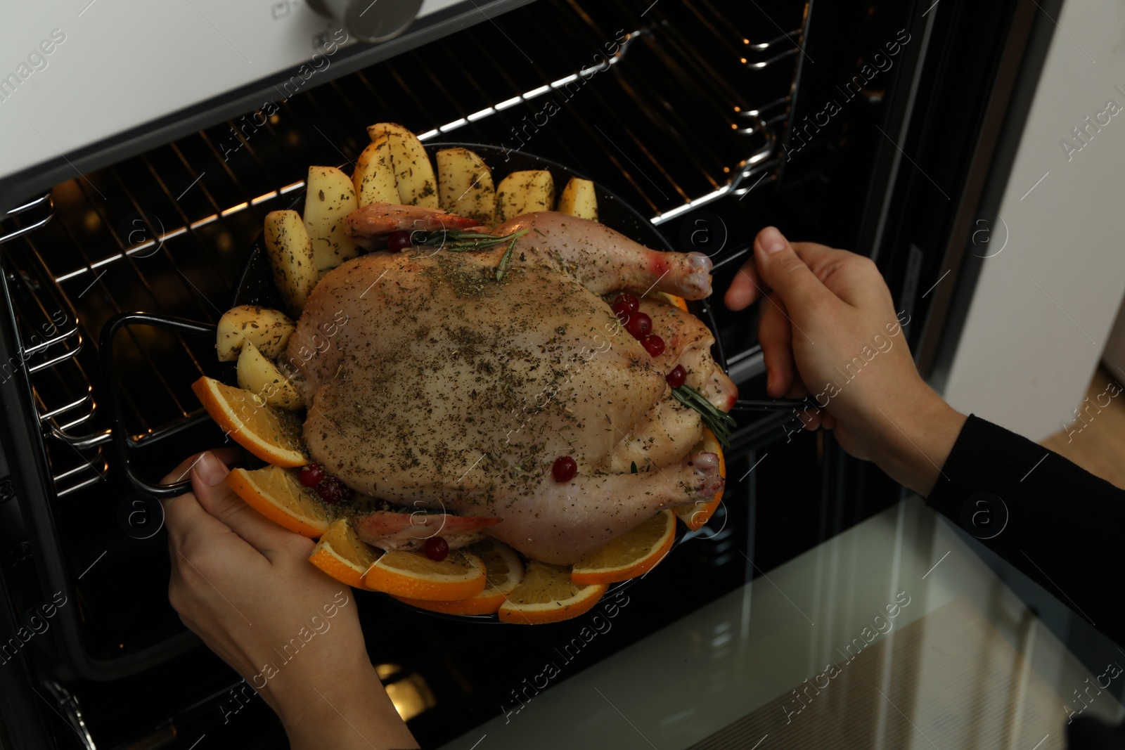 Photo of Woman putting chicken with orange and potato slices into oven, closeup