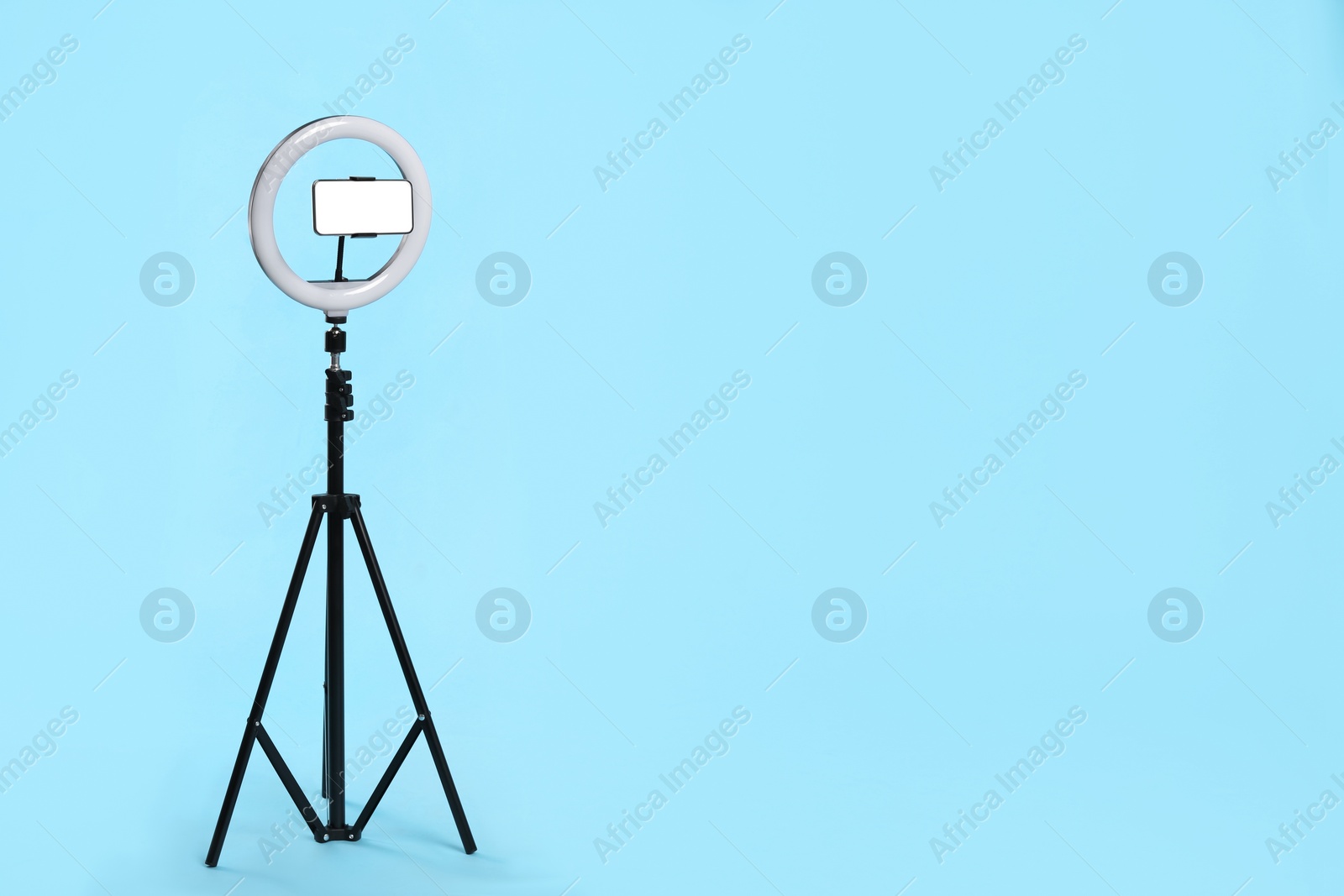 Photo of Modern tripod with ring light and smartphone on light blue background. Space for text