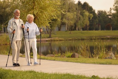 Senior man and woman performing Nordic walking outdoors, space for text