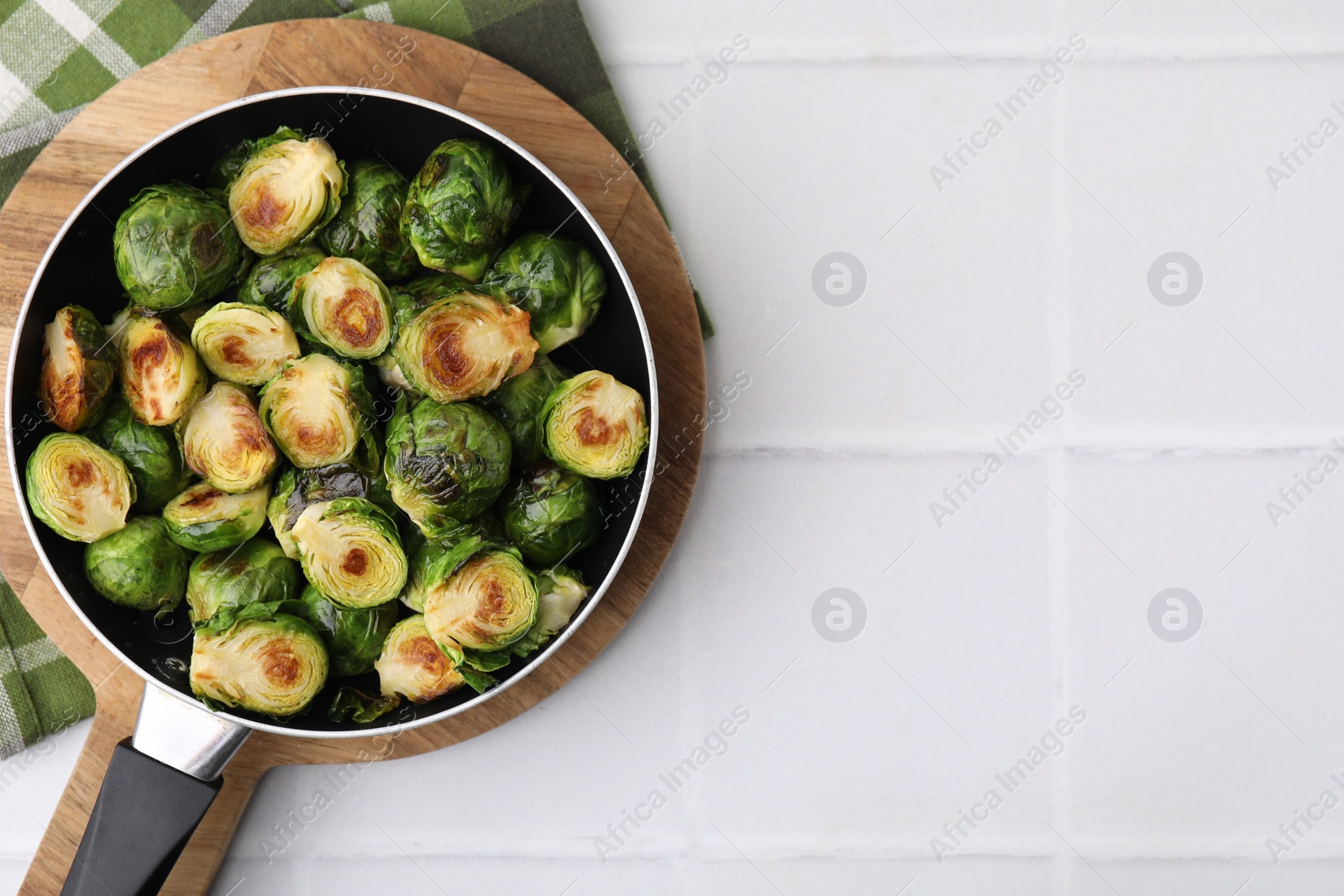 Photo of Delicious roasted Brussels sprouts in frying pan on white tiled table, top view. Space for text