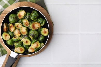 Photo of Delicious roasted Brussels sprouts in frying pan on white tiled table, top view. Space for text