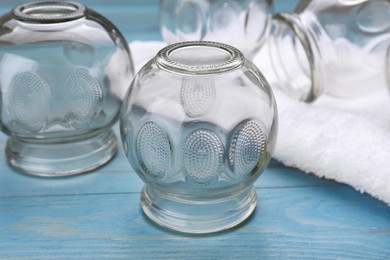 Photo of Glass cups and towel on light blue wooden table, closeup. Cupping therapy
