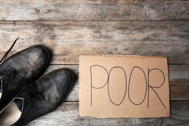 Dirty shoes and carton sign with word POOR on wooden background, top view