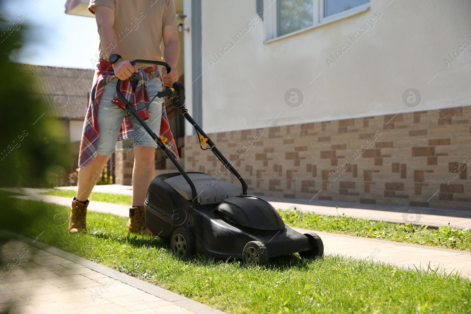 Photo of Man cutting green grass with lawn mower on backyard, closeup