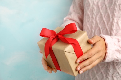 Photo of Woman holding beautiful Christmas gift on light blue background, closeup