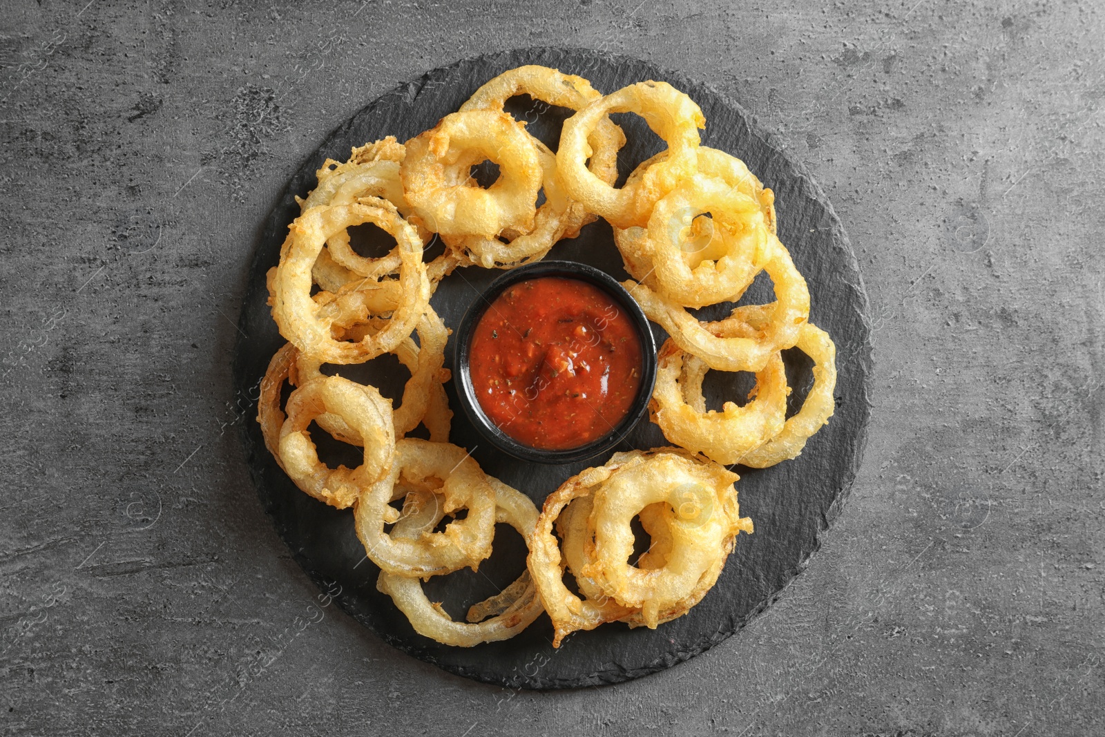 Photo of Delicious golden crispy onion rings and sauce on gray background, top view