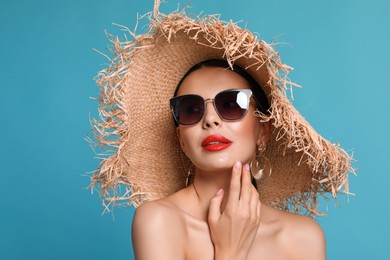 Photo of Attractive woman in fashionable sunglasses and wicker hat against light blue background