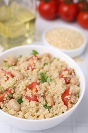 Delicious quinoa salad with tomatoes, beans and parsley served on white tiled table, closeup