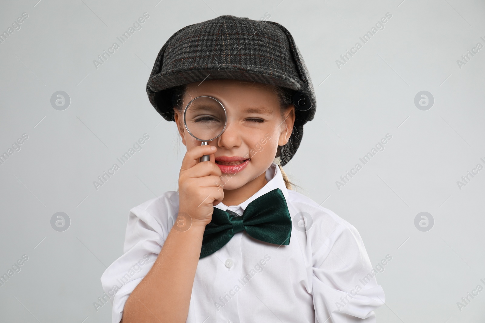 Photo of Cute little detective with magnifying glass on grey background