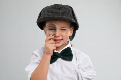 Photo of Cute little detective with magnifying glass on grey background