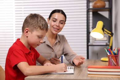 Photo of Dyslexia problem. Mother helping son with homework at table indoors, selective focus