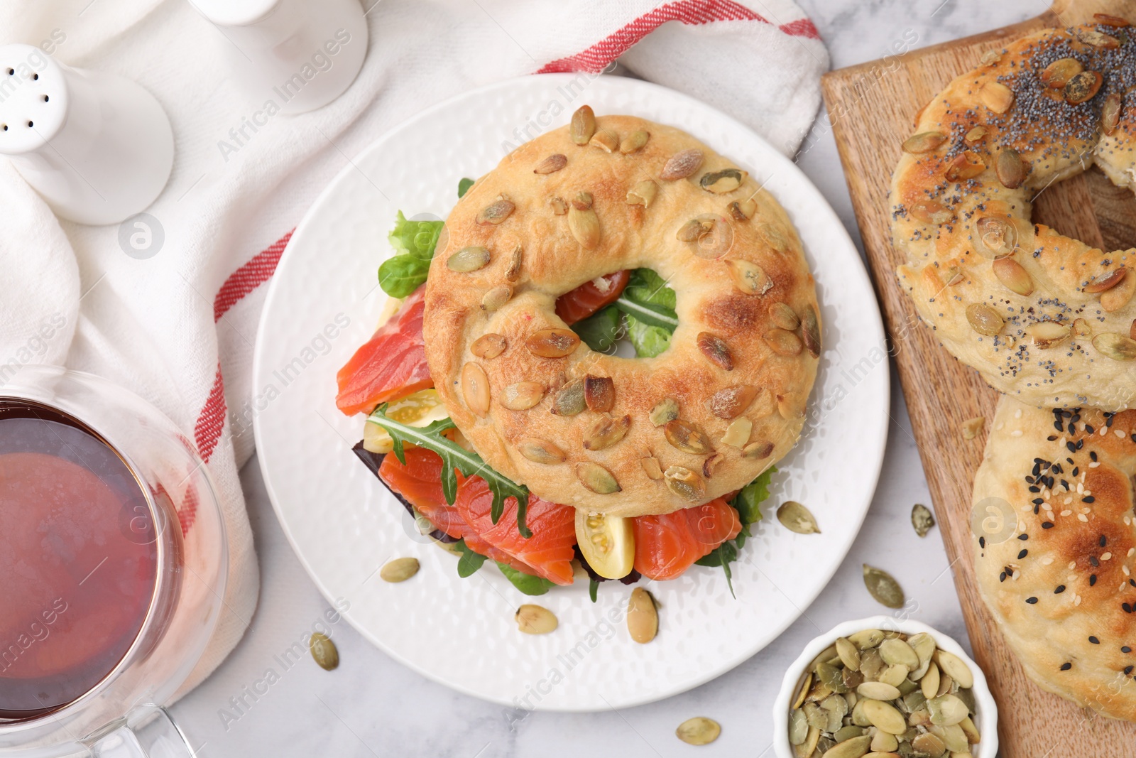 Photo of Tasty bagel with salmon and tomatoes on white marble table, flat lay