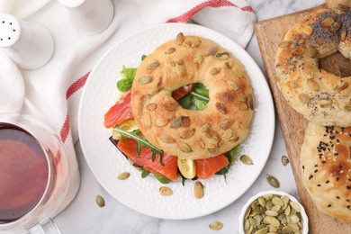 Tasty bagel with salmon and tomatoes on white marble table, flat lay