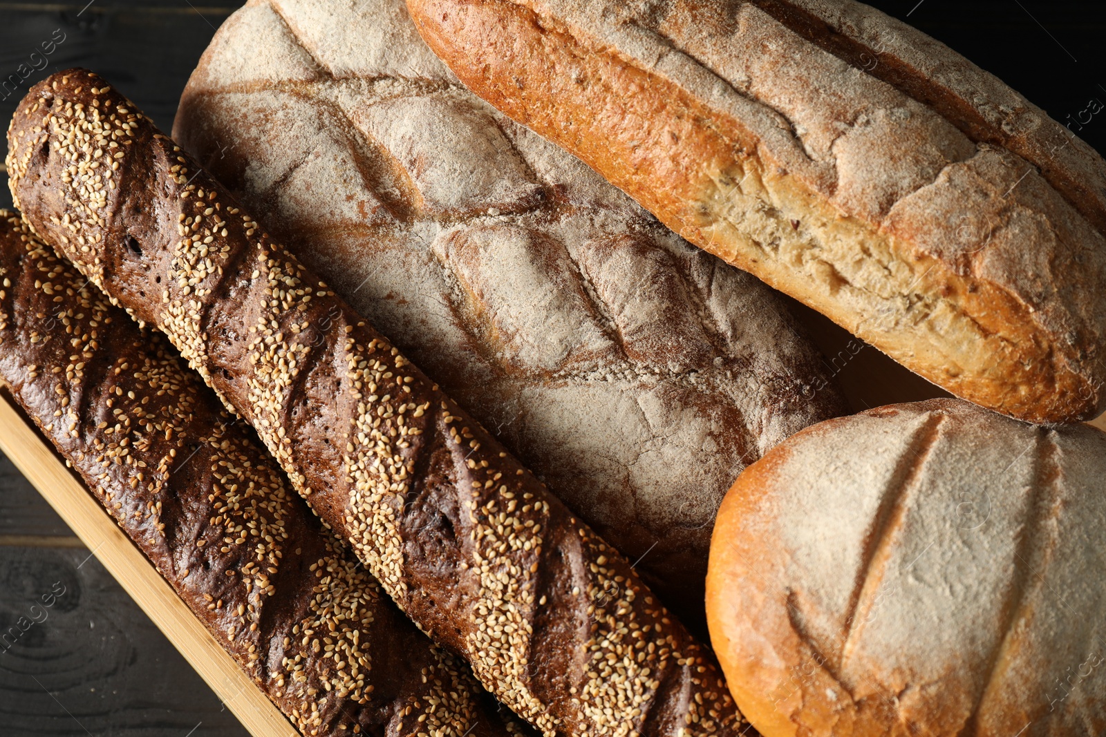 Photo of Basket with different types of fresh bread on black wooden table, top view