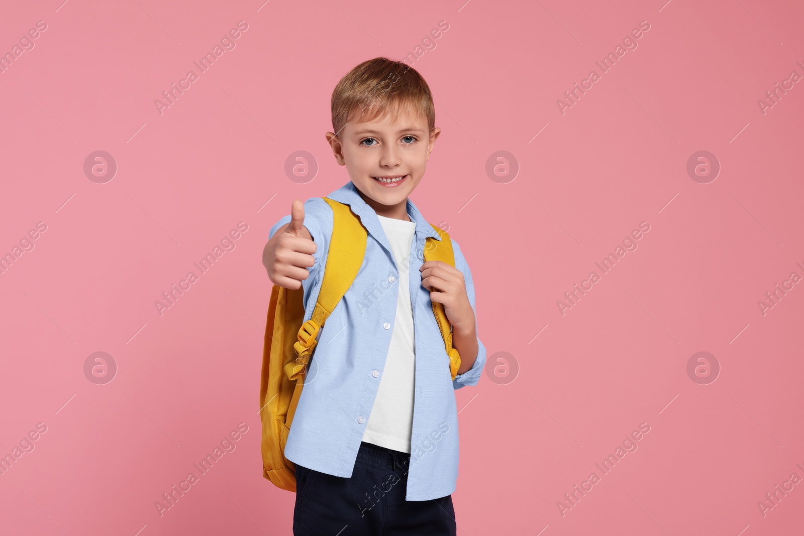 Photo of Happy schoolboy with backpack showing thumb up gesture on pink background