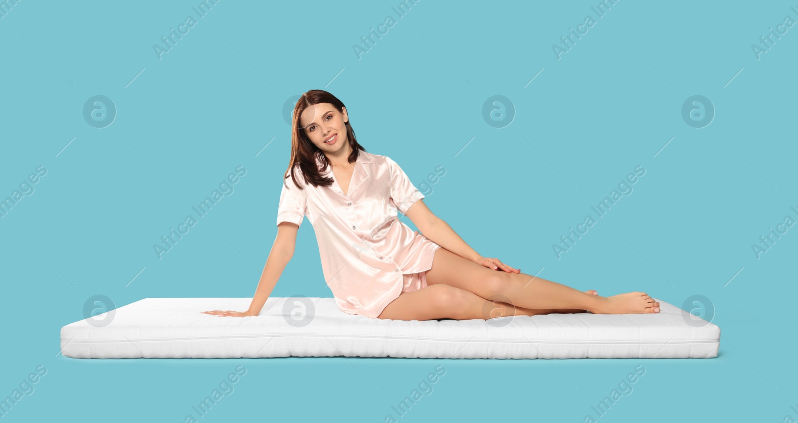 Photo of Young woman sitting on soft mattress against light blue background