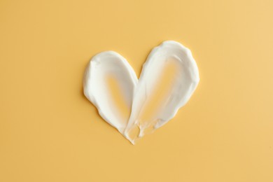 Photo of Samples of face cream in shape of heart on yellow background, top view