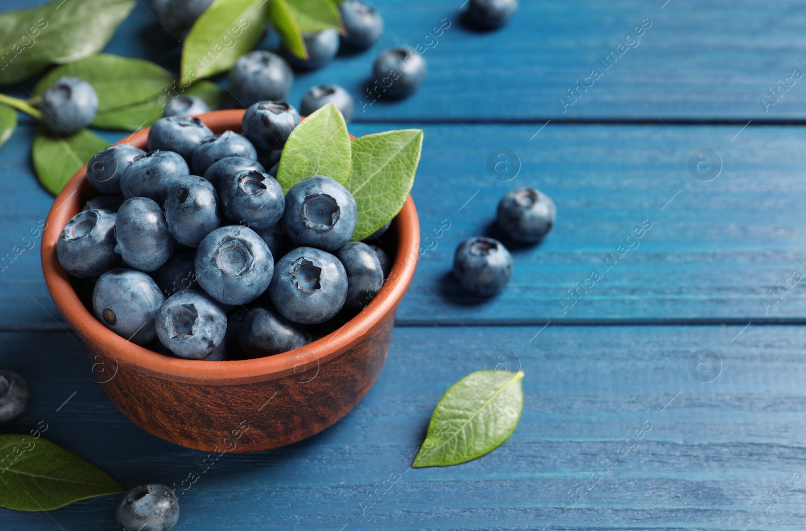 Photo of Tasty fresh blueberries in bowl on blue wooden table, space for text