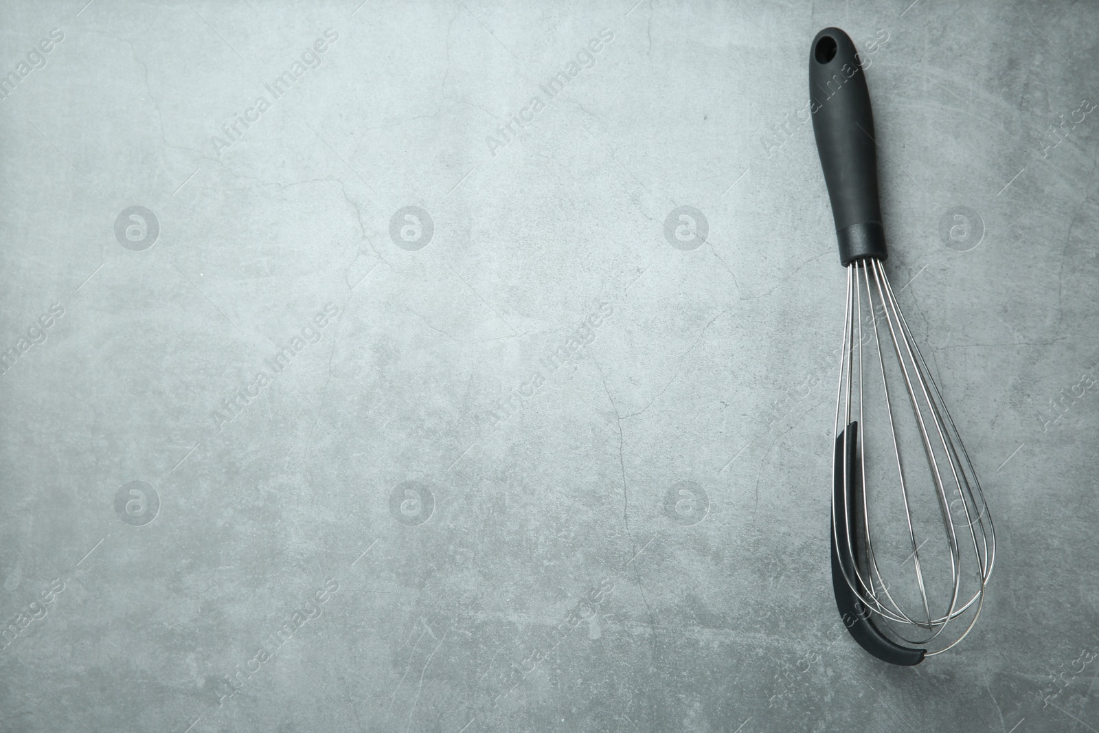 Photo of Metal whisk on gray table, top view. Space for text