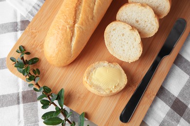 Photo of Cut baguette with fresh butter on checkered tablecloth, top view