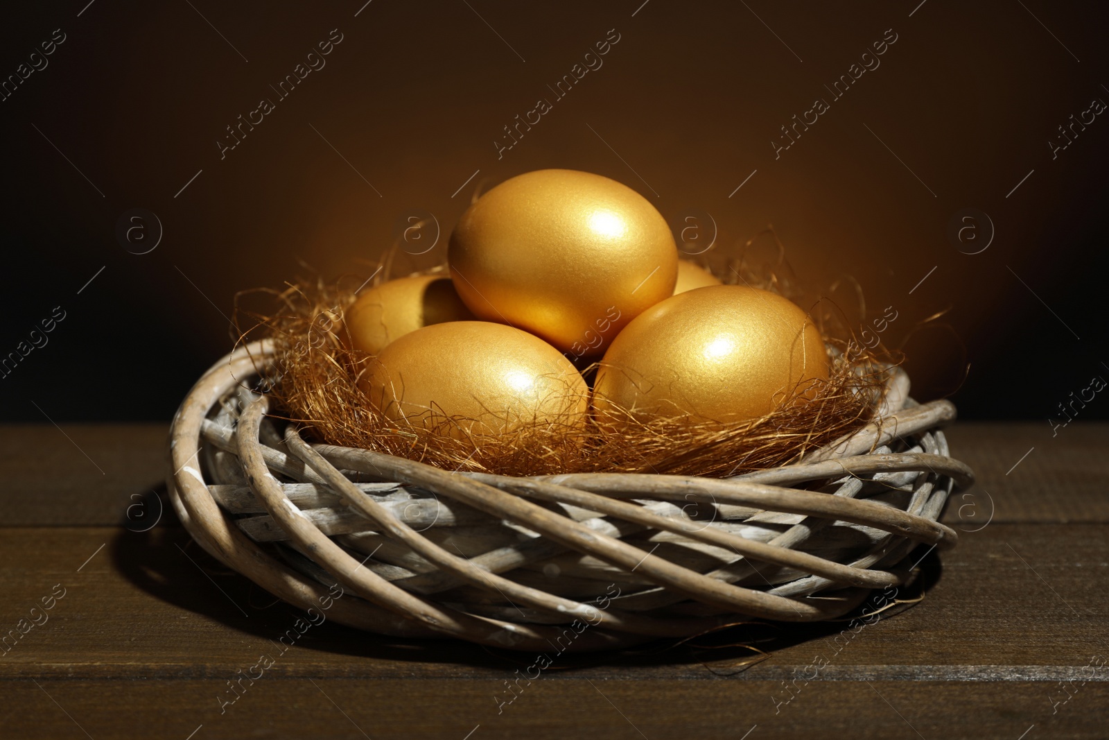 Photo of Shiny golden eggs in nest on wooden table