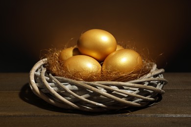 Photo of Shiny golden eggs in nest on wooden table