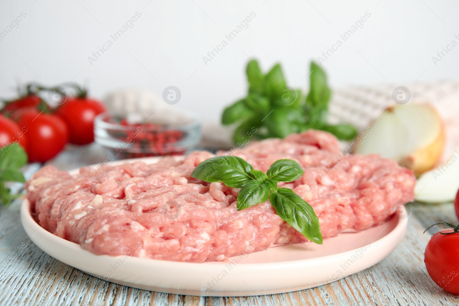 Photo of Raw chicken minced meat with basil on light blue wooden table, closeup