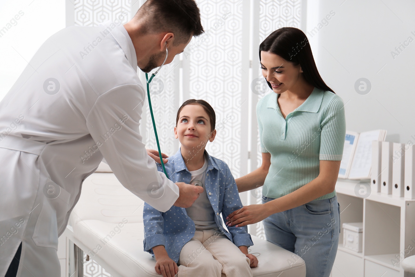 Photo of Mother with daughter visiting pediatrician in hospital. Doctor examining little girl