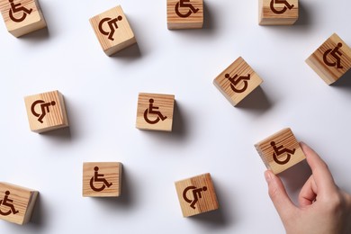 Image of Inclusion concept. Woman arranging wooden cubes with international symbols of access on white background, top view
