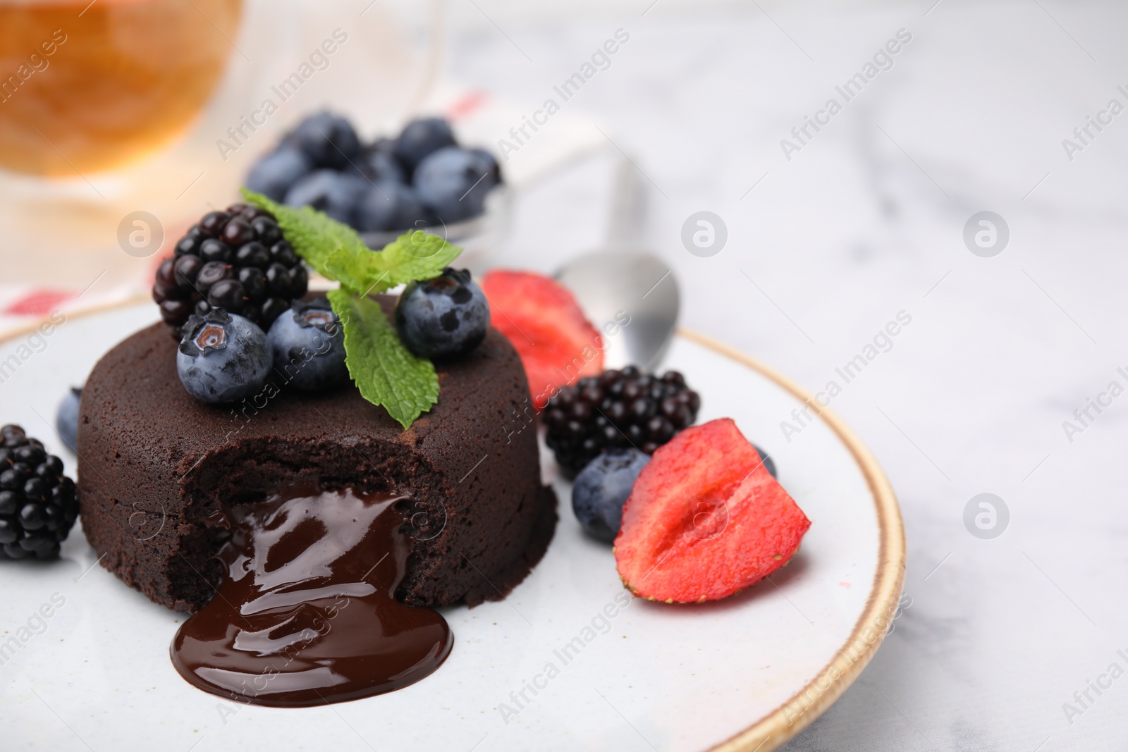 Photo of Plate with delicious chocolate fondant, berries and mint on white marble table, closeup. Space for text