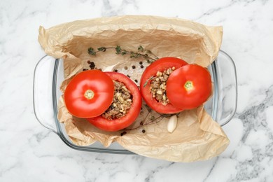 Uncooked stuffed tomatoes with minced beef, bulgur and mushrooms in baking dish on white marble table, top view