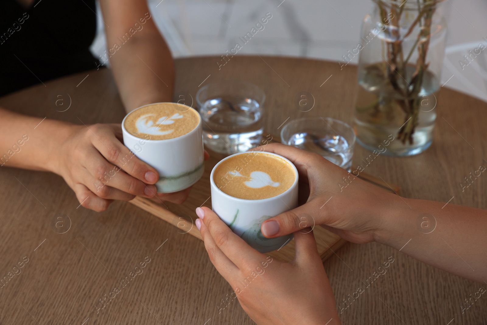 Photo of Friends drinking coffee at wooden table in cafe, closeup