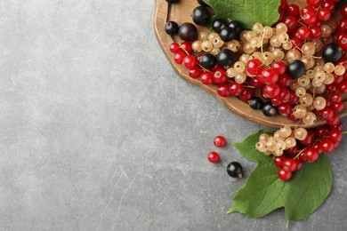 Photo of Different fresh ripe currants and green leaves on light grey table, top view. Space for text