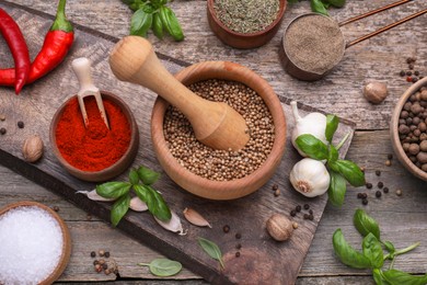 Mortar with pestle and different spices on wooden table, above view