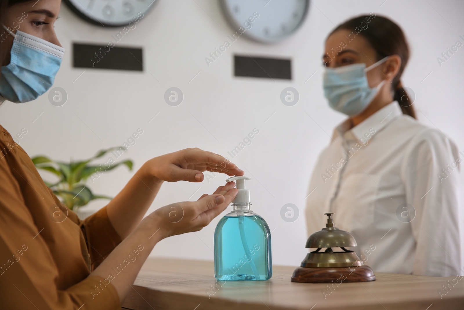 Photo of Woman applying antiseptic gel at hotel reception, closeup