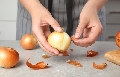 Photo of Young woman peeling ripe onion at grey table, closeup