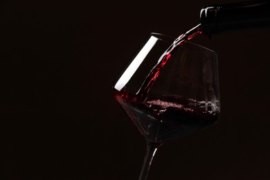 Photo of Pouring red wine into glass against black background, closeup. Space for text