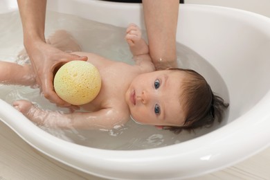 Mother bathing her little baby with sponge in bathtub, closeup
