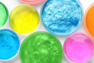 Photo of Colorful slimes in plastic containers on white background, top view. Antistress toy